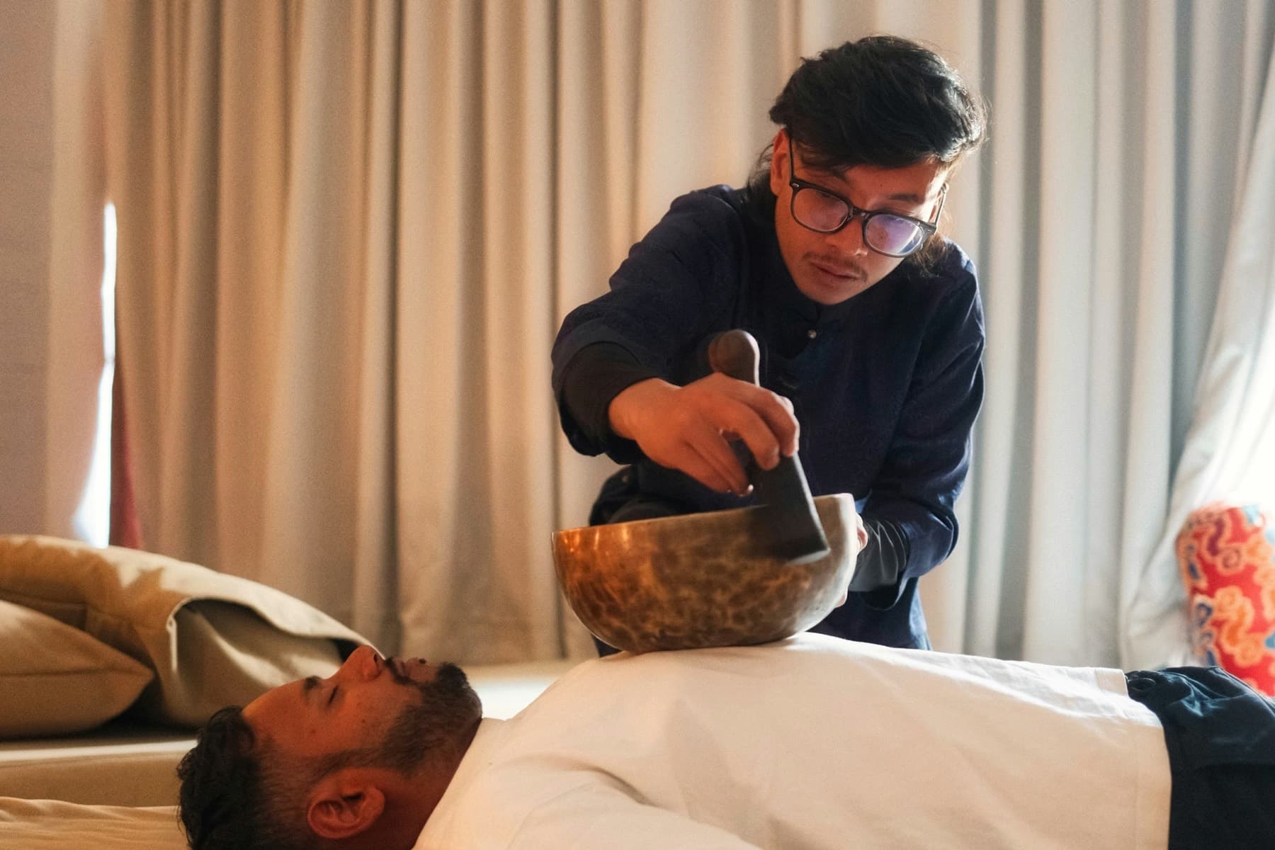 A sound practitioner playing a bronze singing bowl during a relaxation session