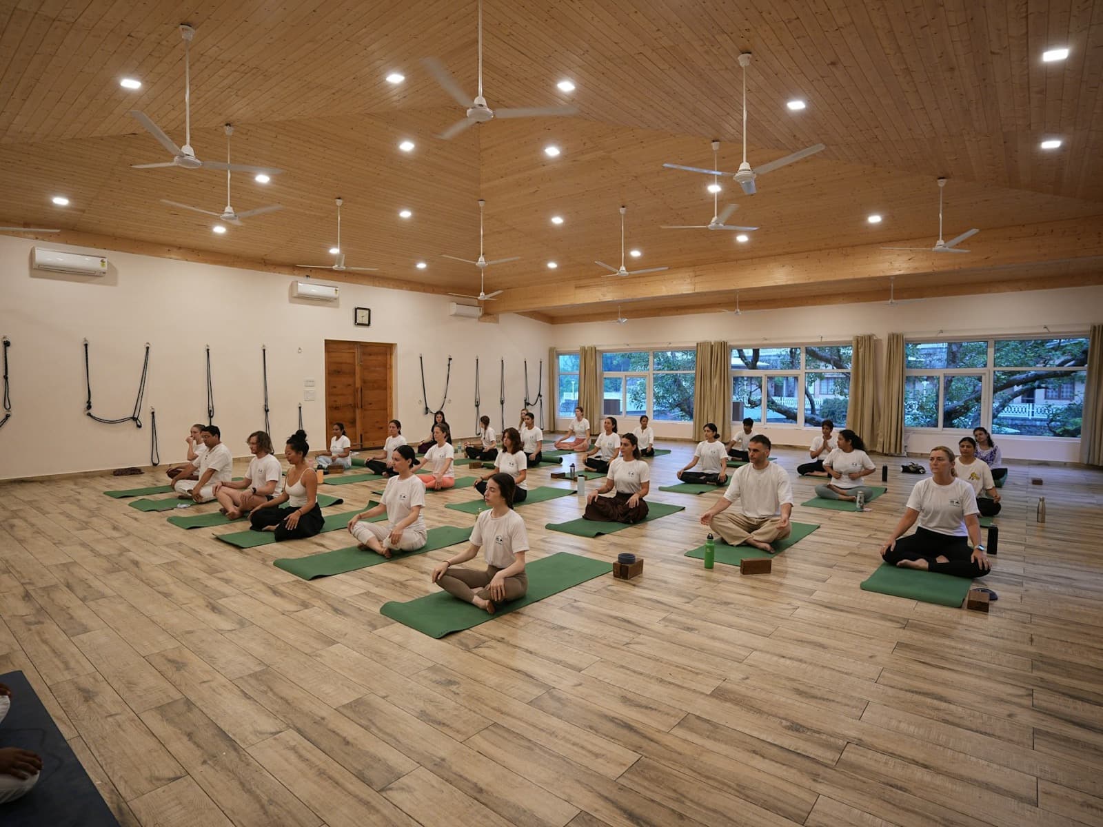 A large group practising seated meditation together in a bright hall